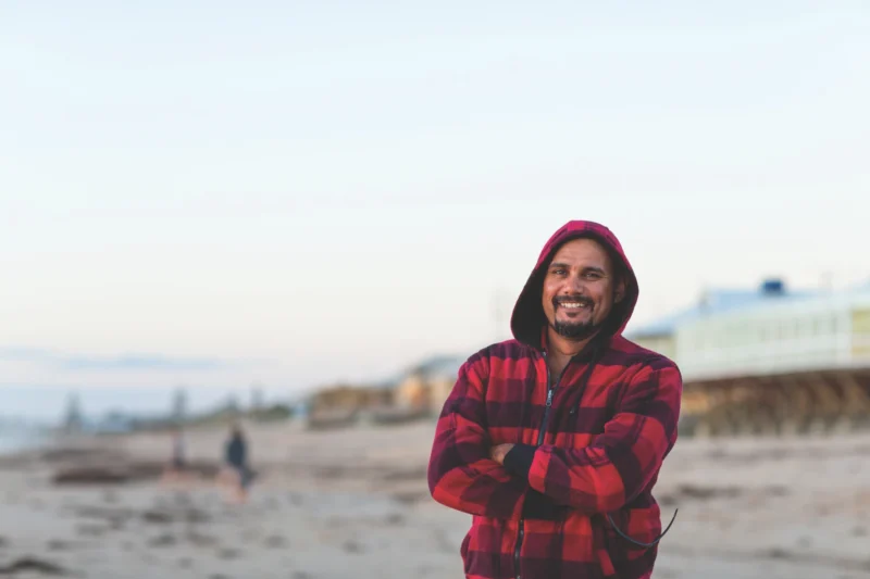 Man standing on the beach smiling for a photo from one of Anglicare's chaplaincy programs.
