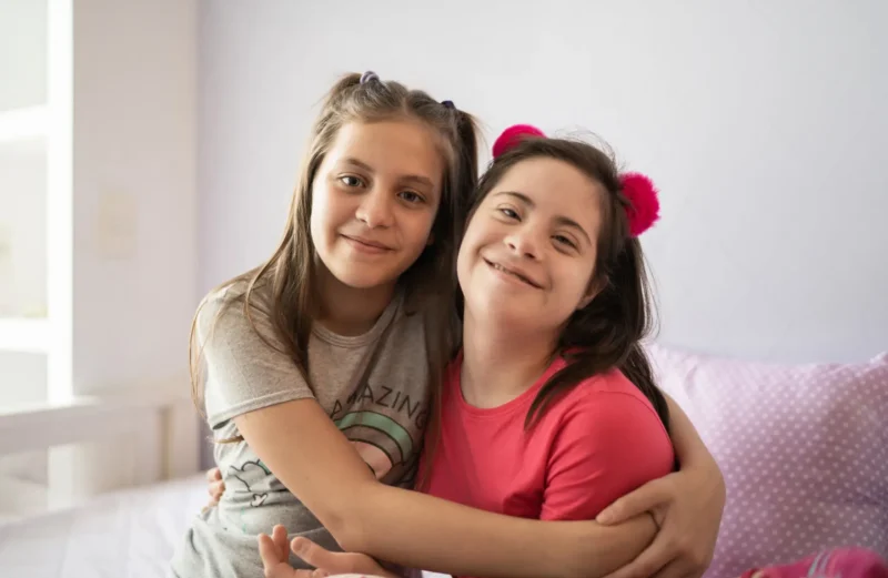 Teenage foster child hugging another sister with a disability.