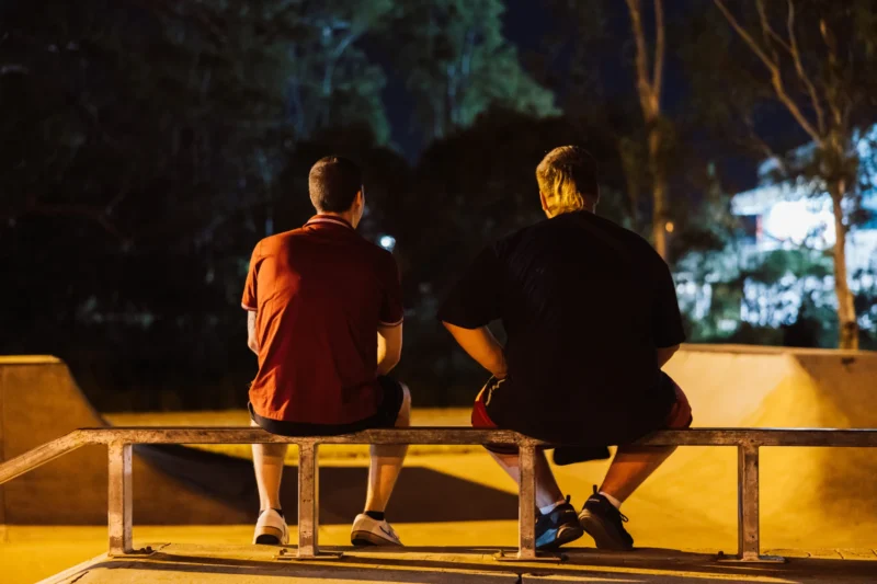 Male youth homelessness service client sitting outside at night talking with an Anglicare support worker, illustrating outreach and connection.