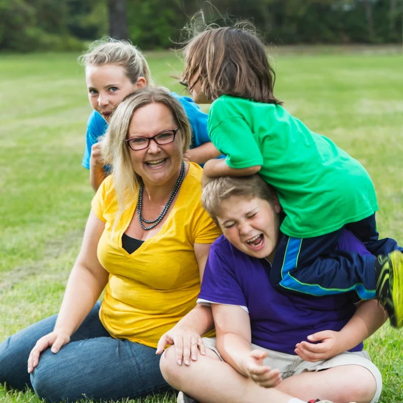 Foster mum sitting on grass being hugged by three children