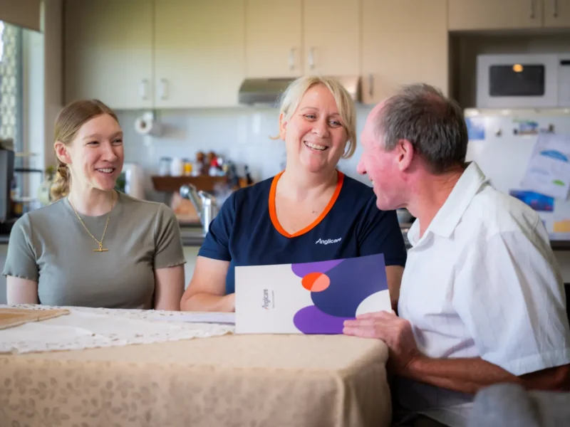 Anglicare worker, client and his daughter sitting at a table going through aged care funding options.