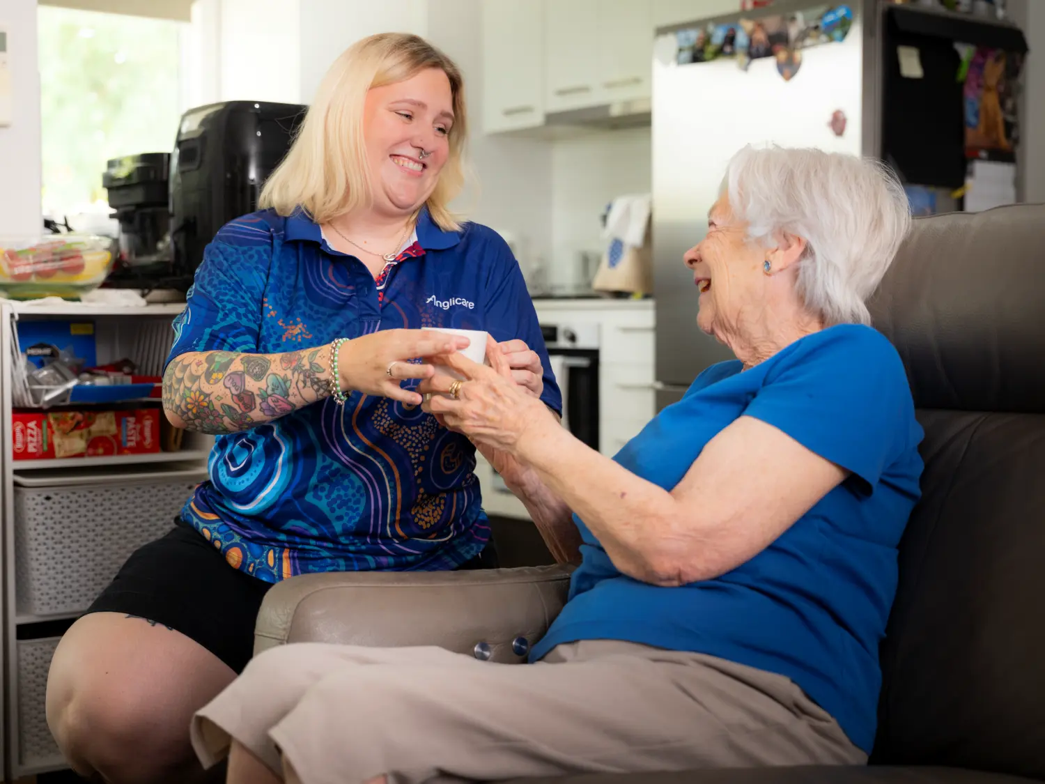 In-home worker supporting elderly by bringing her tea.