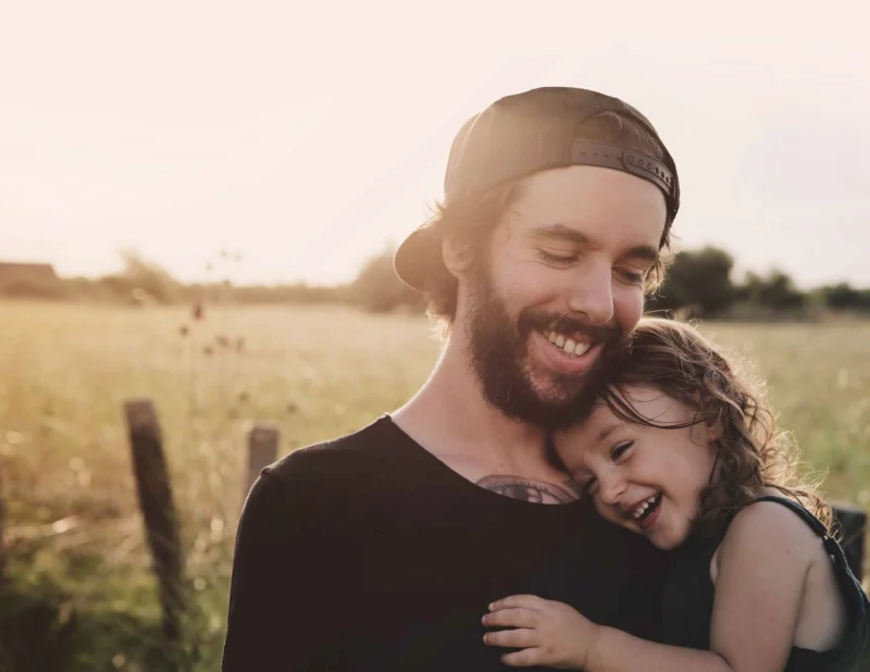 Foster parenting hugging a child outside with field behind them.