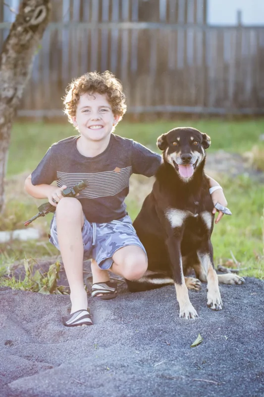 Young foster child with his arm around dog and smiling at the camera.