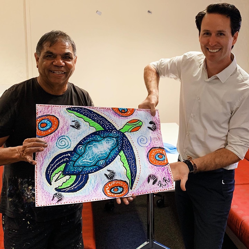 Anglicare staff member and First Nations artist holding up artwork of a turtle for NAIDOC Week 2019