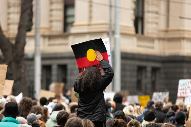 First Nations lady holding up picture of Aboriginal flag in a rally.