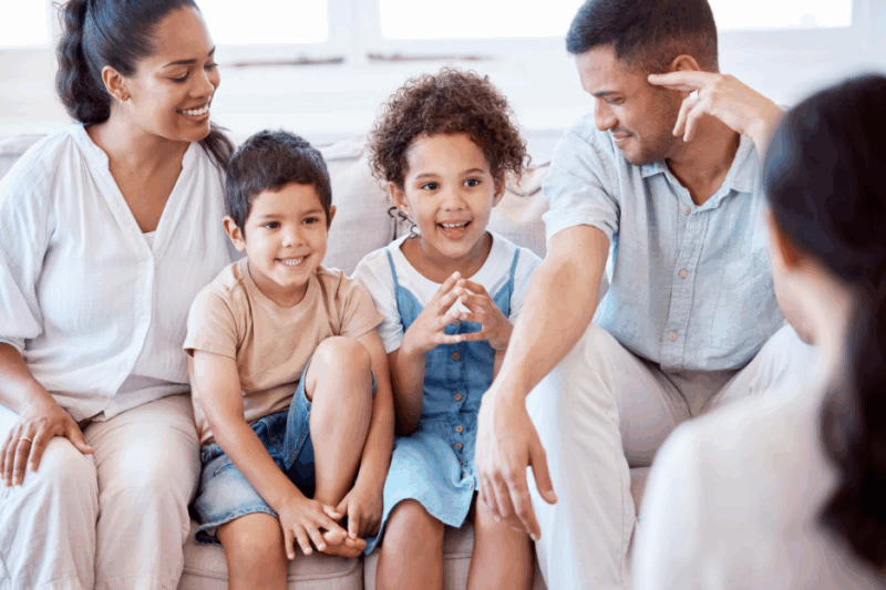 A young family with two children sitting down to do family counselling with a female counsellor