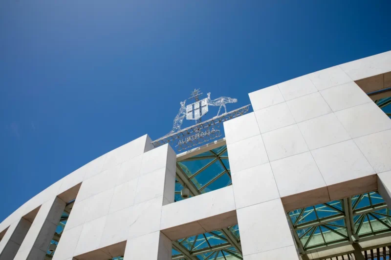 Australian Parliament House exterior under a clear blue sky, representing government policy challenges impacting youth homelessness services in Australia.