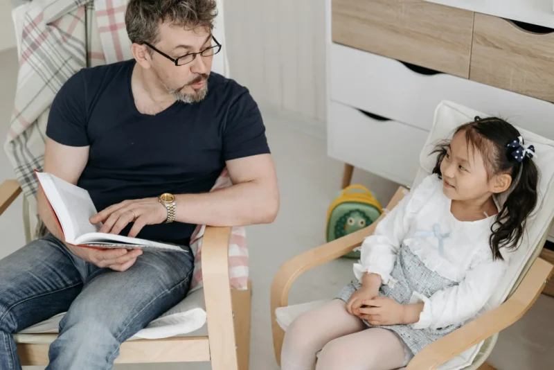 Foster carer reading and talking with a young child in a calm home setting, reflecting the emotional support and stability offered through foster care services